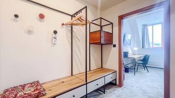 A bedroom with a wooden bed, a bench with drawers, a hanging clothes rack, and a desk with a chair.