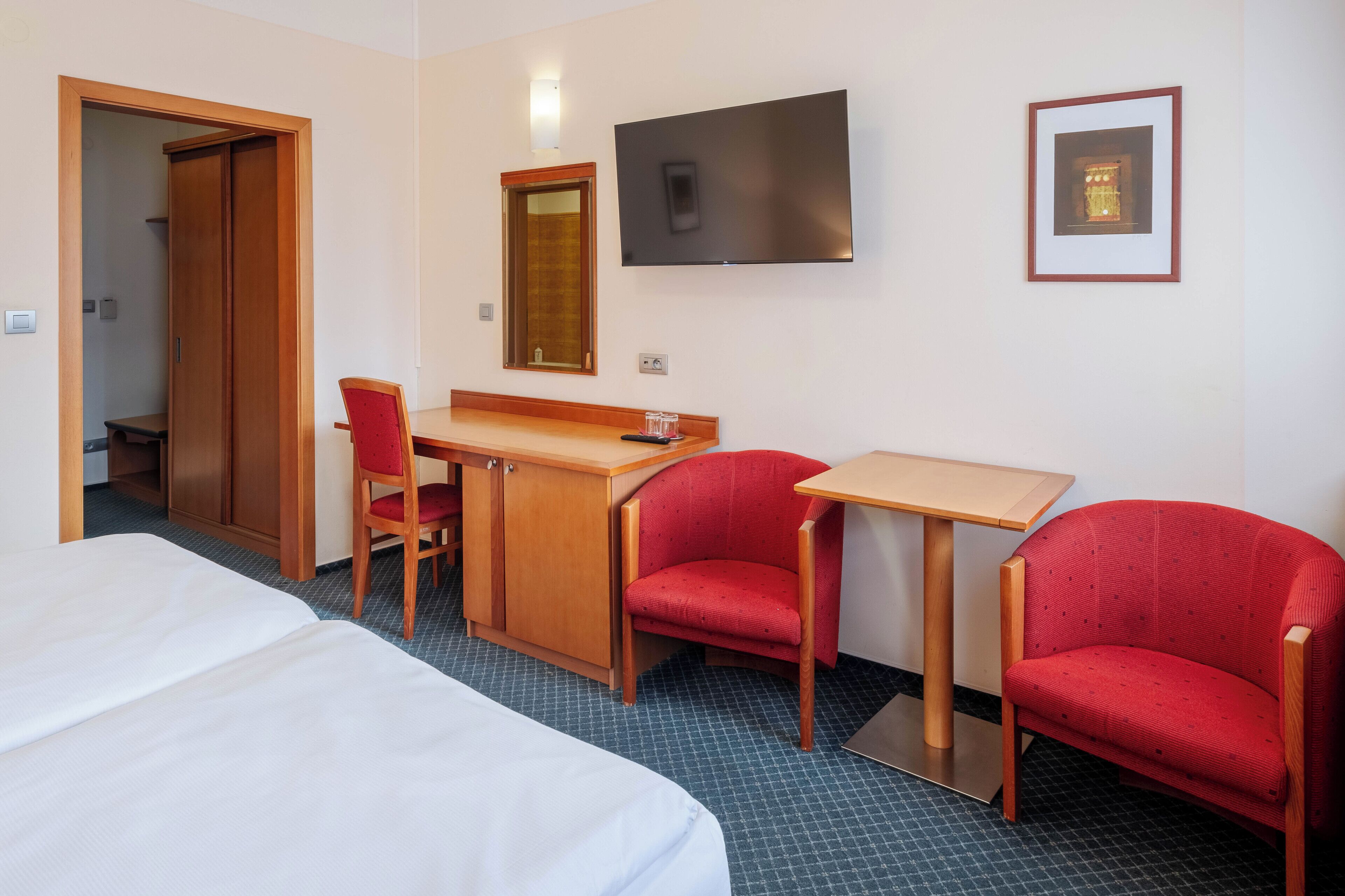 Une chambre d’hôtel avec un lit, un bureau et une chaise, une télévision et un tableau encadré au mur.