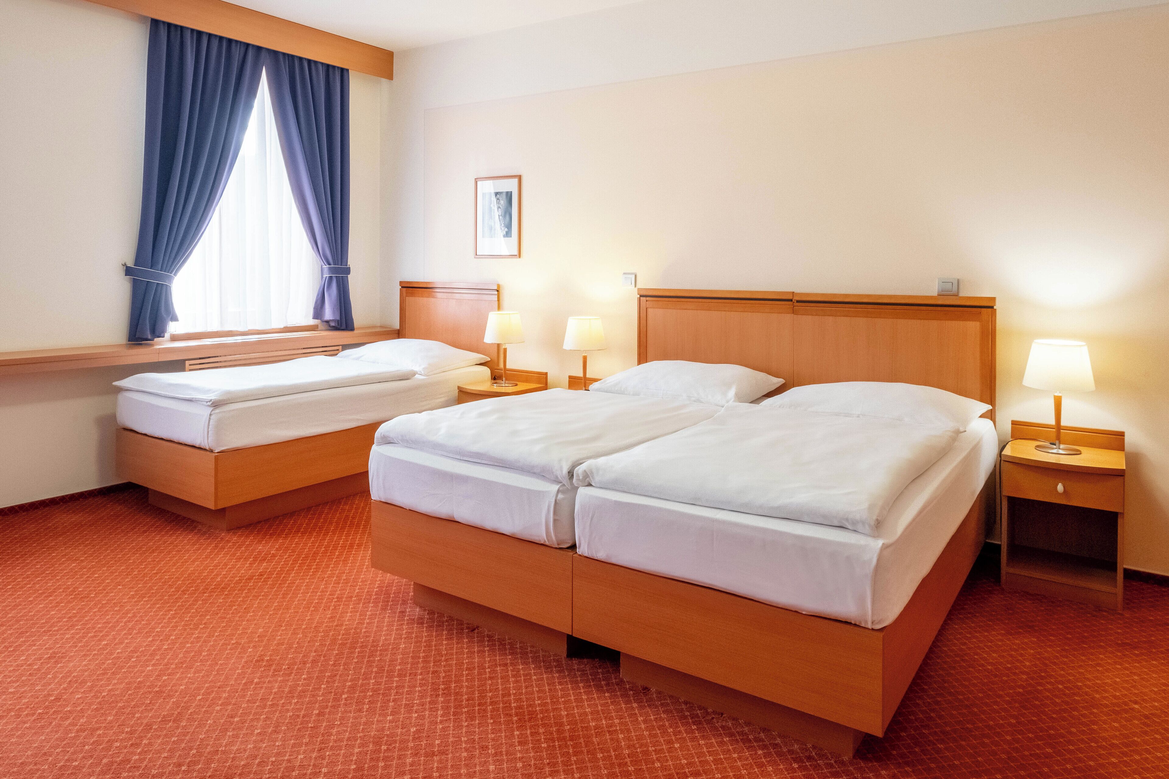 A hotel room with two beds, a window with curtains, bedside lamps, and a framed picture on the wall.