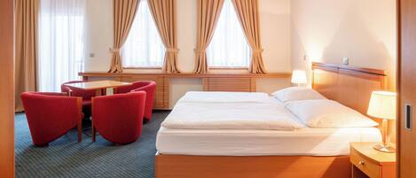 Habitación de hotel con cama doble, un escritorio con silla y dos sillones rojos.