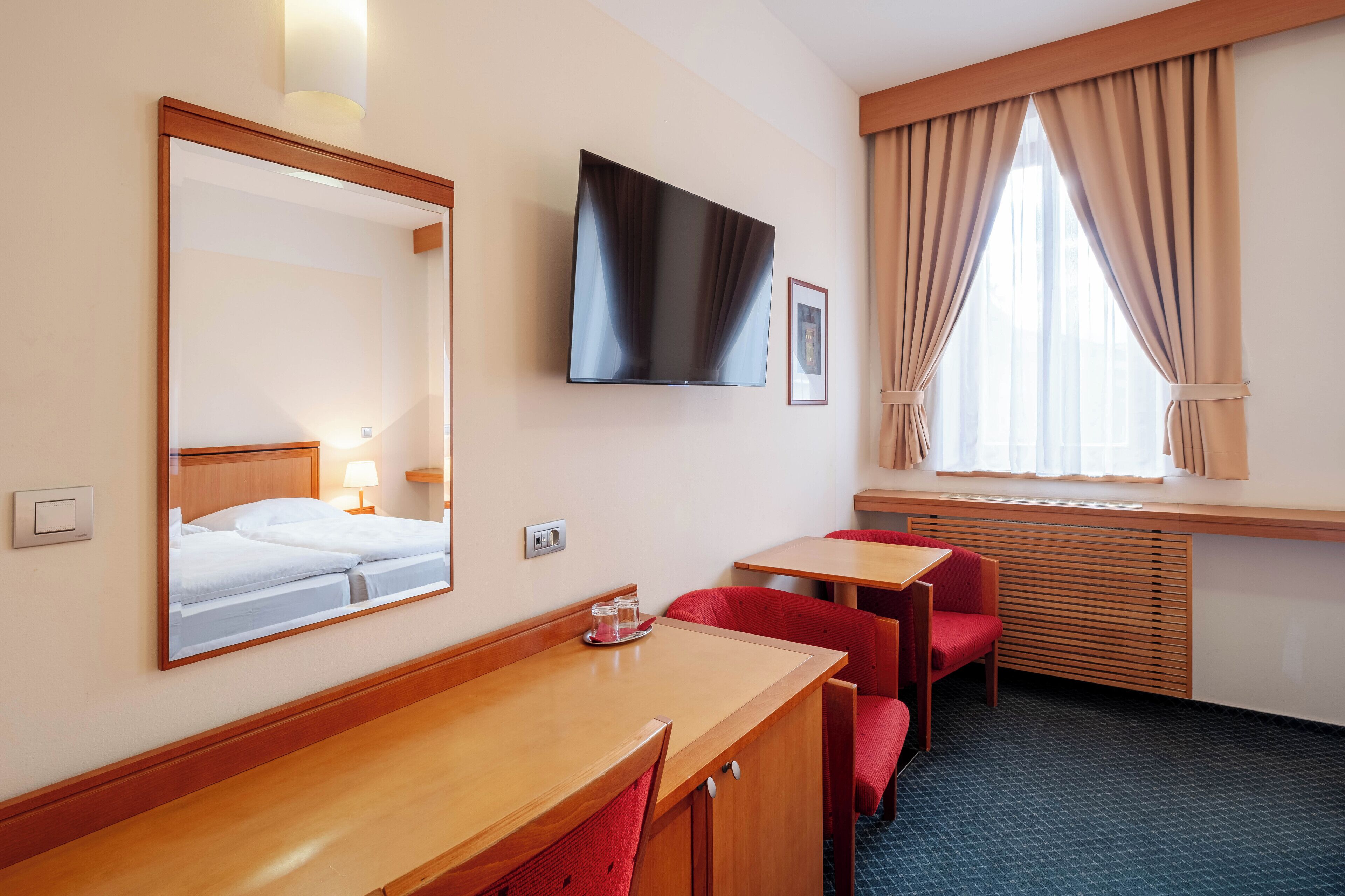 Une chambre d’hôtel avec un lit, une télévision, un bureau et une fenêtre avec des rideaux.