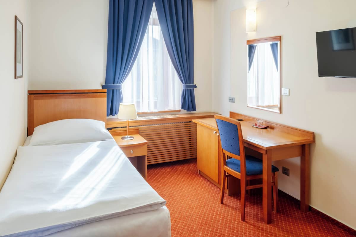 Una habitación de hotel con una cama, un escritorio con una silla, una lámpara, un televisor y un ventanal con cortinas.
