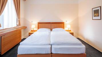 A double bed with wooden headboard, two bedside tables with lamps, a window with curtains, and a framed picture on the wall.