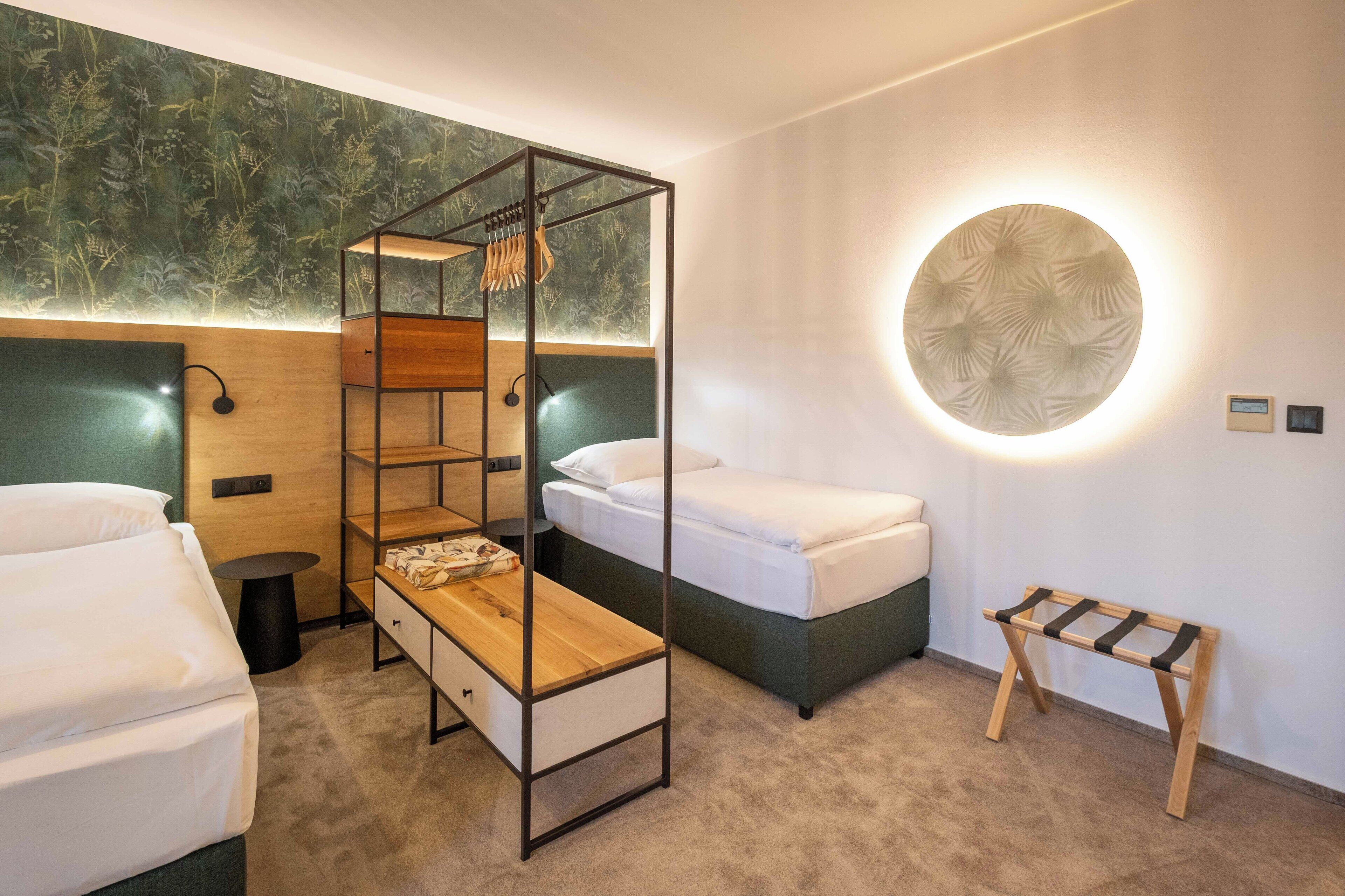 A hotel room with a bunk bed, a bedside table, a wall-mounted lamp, and a circular light fixture.