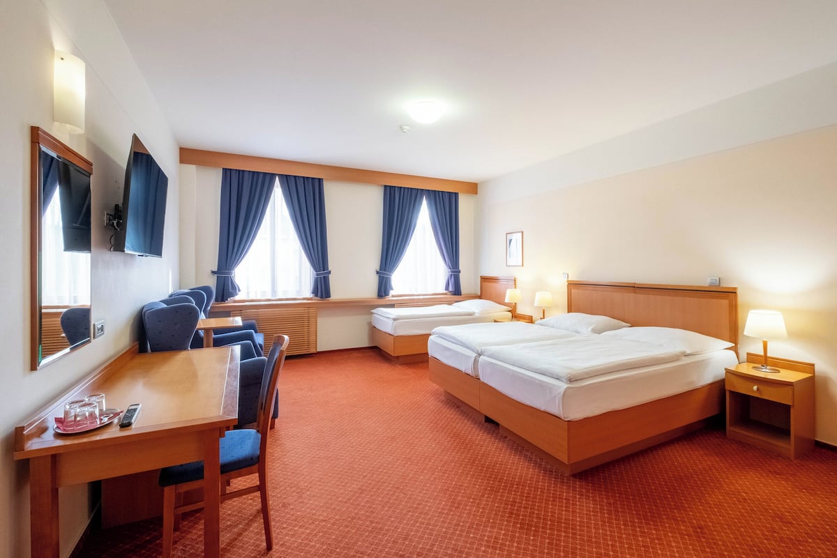 Habitación de hotel con dos camas individuales, un escritorio con silla, una mesita y un televisor.