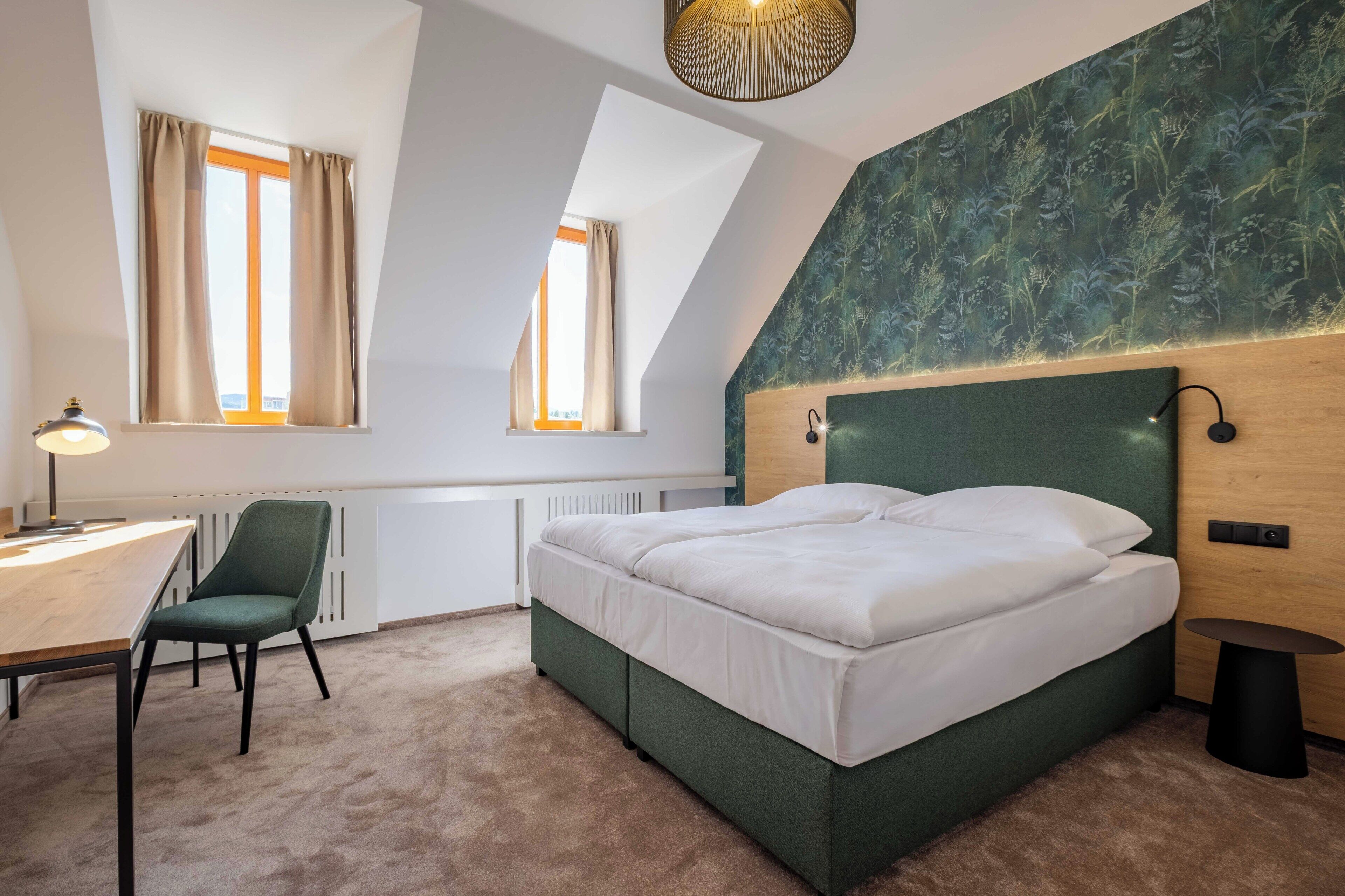 Un dormitorio con cama, escritorio, silla y dos ventanas.