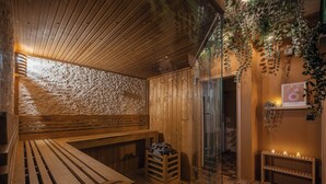 Un sauna en bois avec des bancs et une table-banc, un petit tabouret en bois et une porte en verre donnant sur l’extérieur.