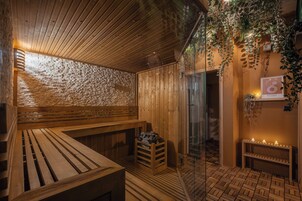 Una sauna de madera con bancos y una mesa-banco, un taburete de madera pequeño, y una puerta de cristal que da al exterior.