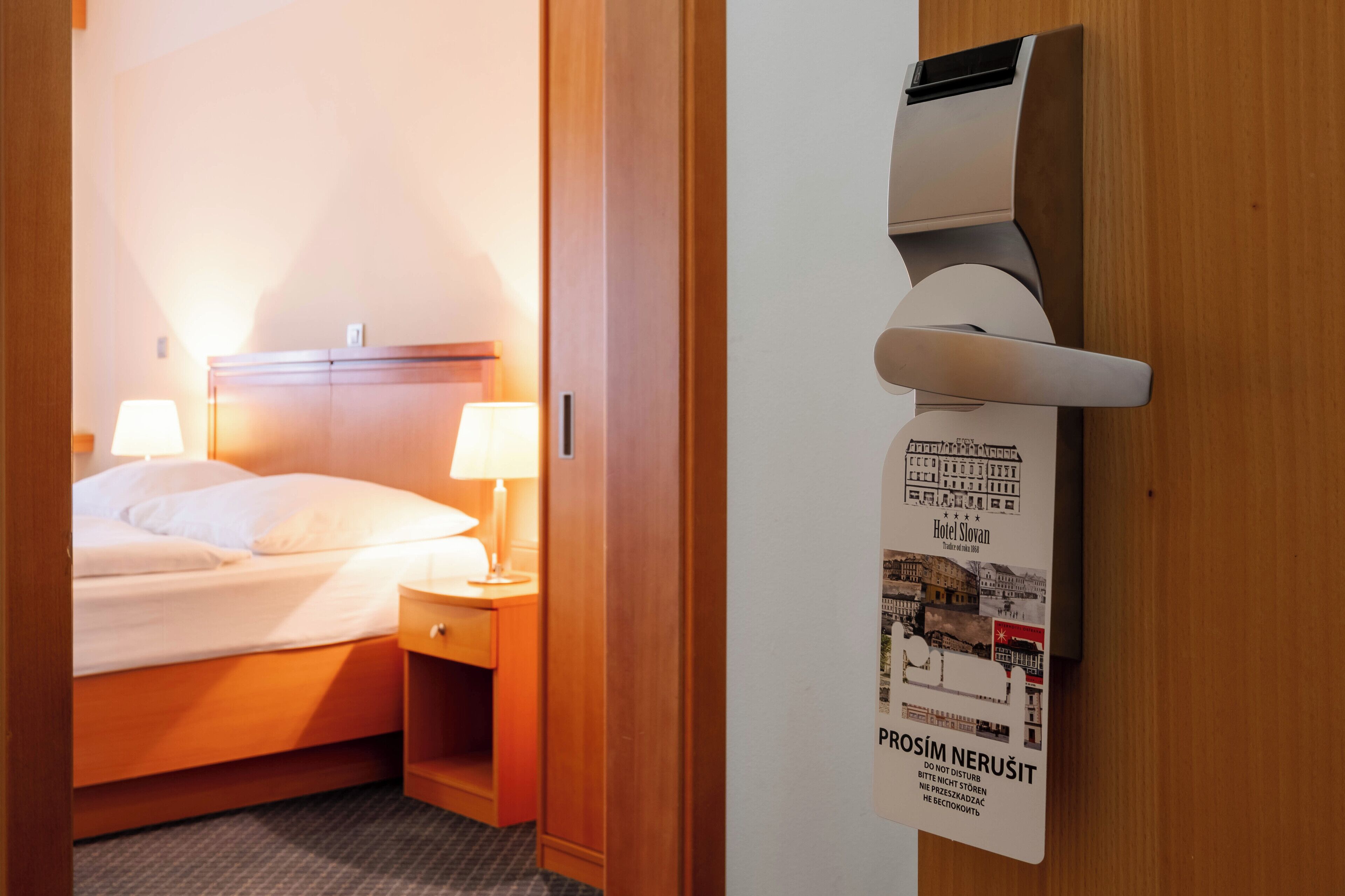 A hotel room with a bed, bedside lamps, a wooden headboard, and a wall-mounted air conditioning unit.