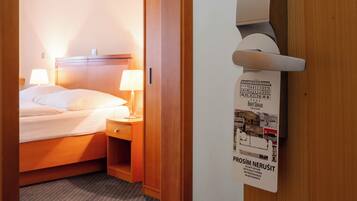 A hotel room with a bed, bedside lamps, a wooden headboard, and a wall-mounted air conditioning unit.