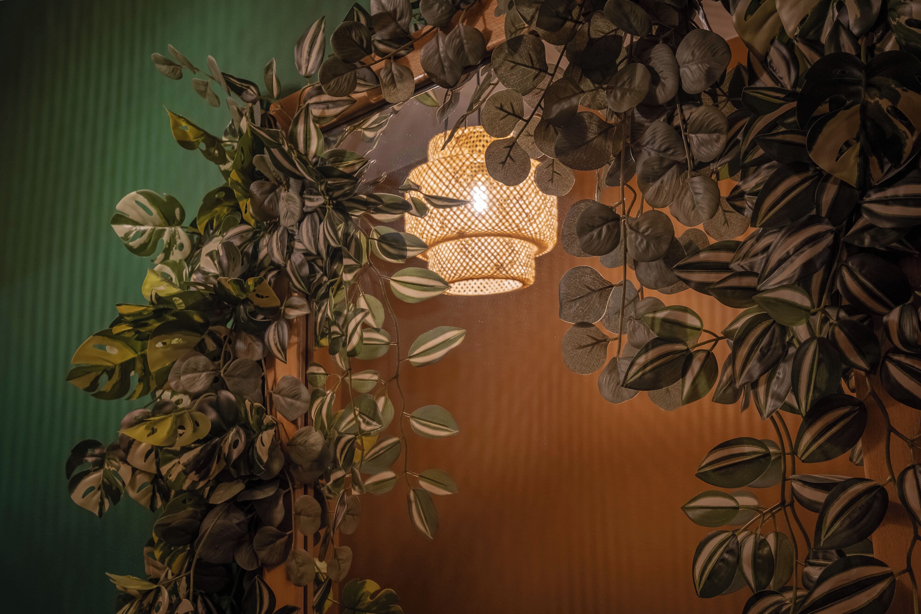 A room with a wooden wall, a hanging light fixture, and dense foliage.
