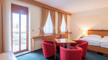 Ein Hotelzimmer mit einem Bett, einem Schreibtisch, zwei roten Stühlen, einem Fenster mit Vorhängen und Blick auf einen Parkplatz.