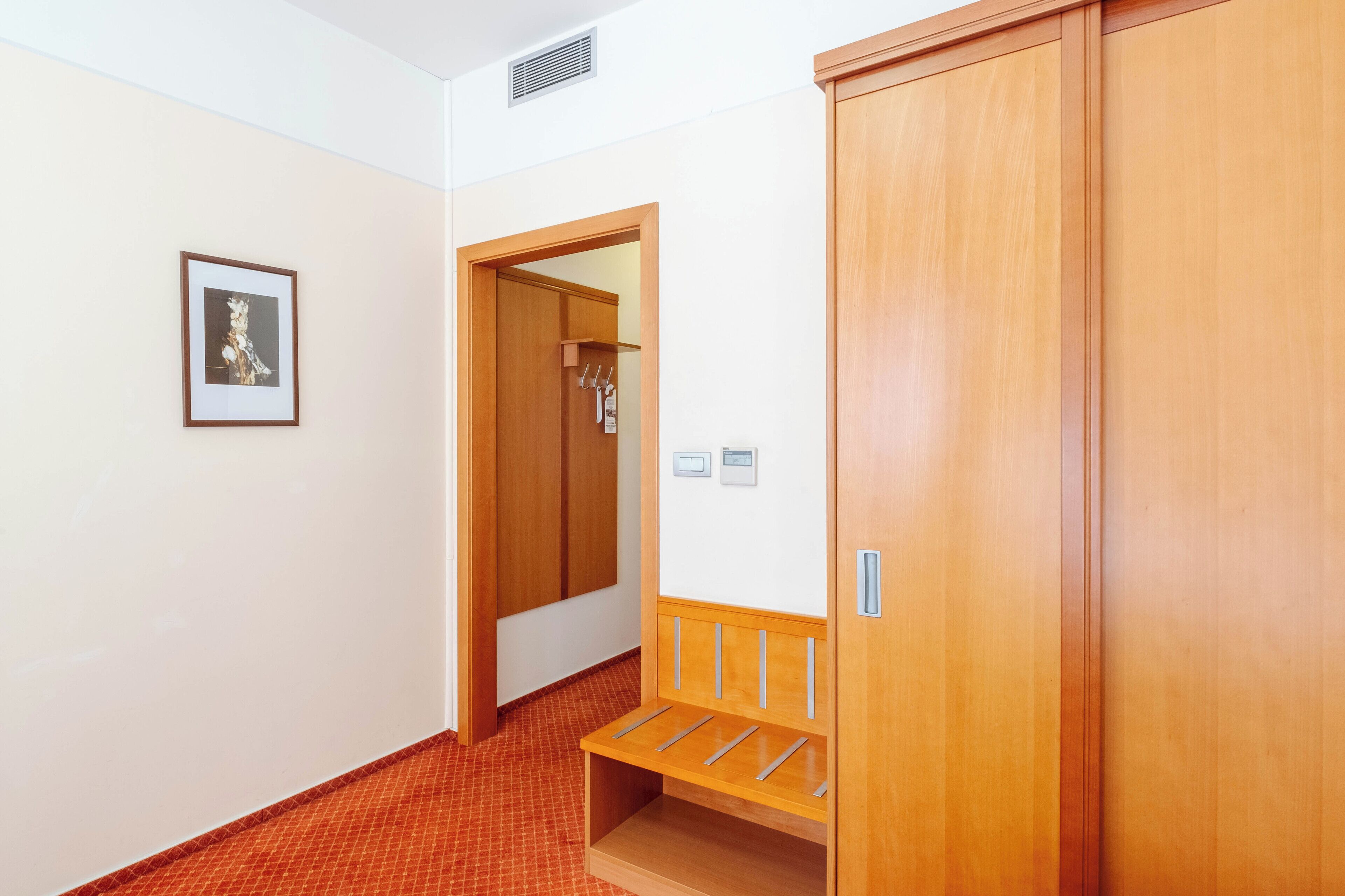 A hallway with a wooden wardrobe, a bench, and a framed picture on the wall.
