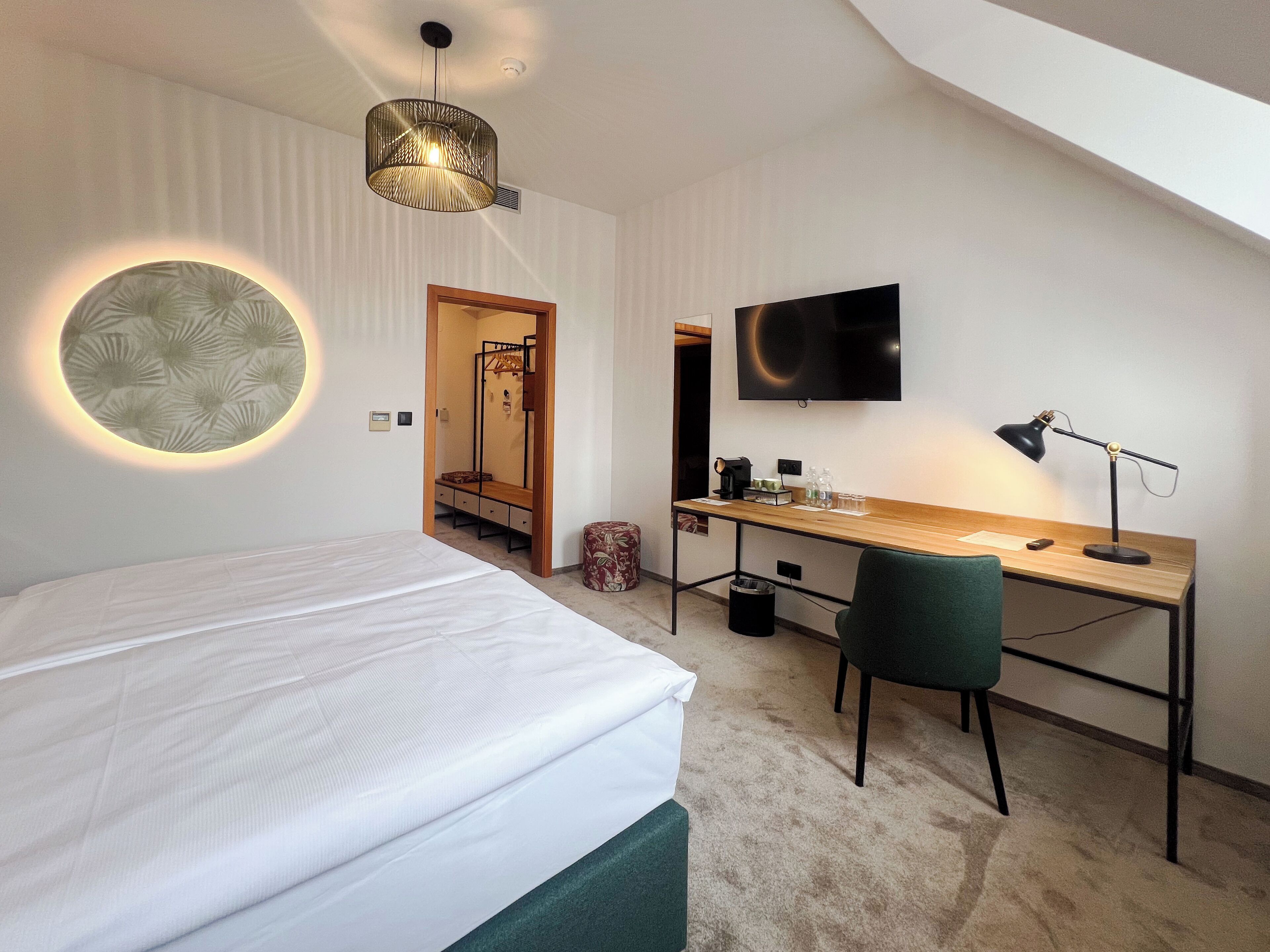 A bedroom with a bed, a desk, a chair, a TV, and a circular light fixture.