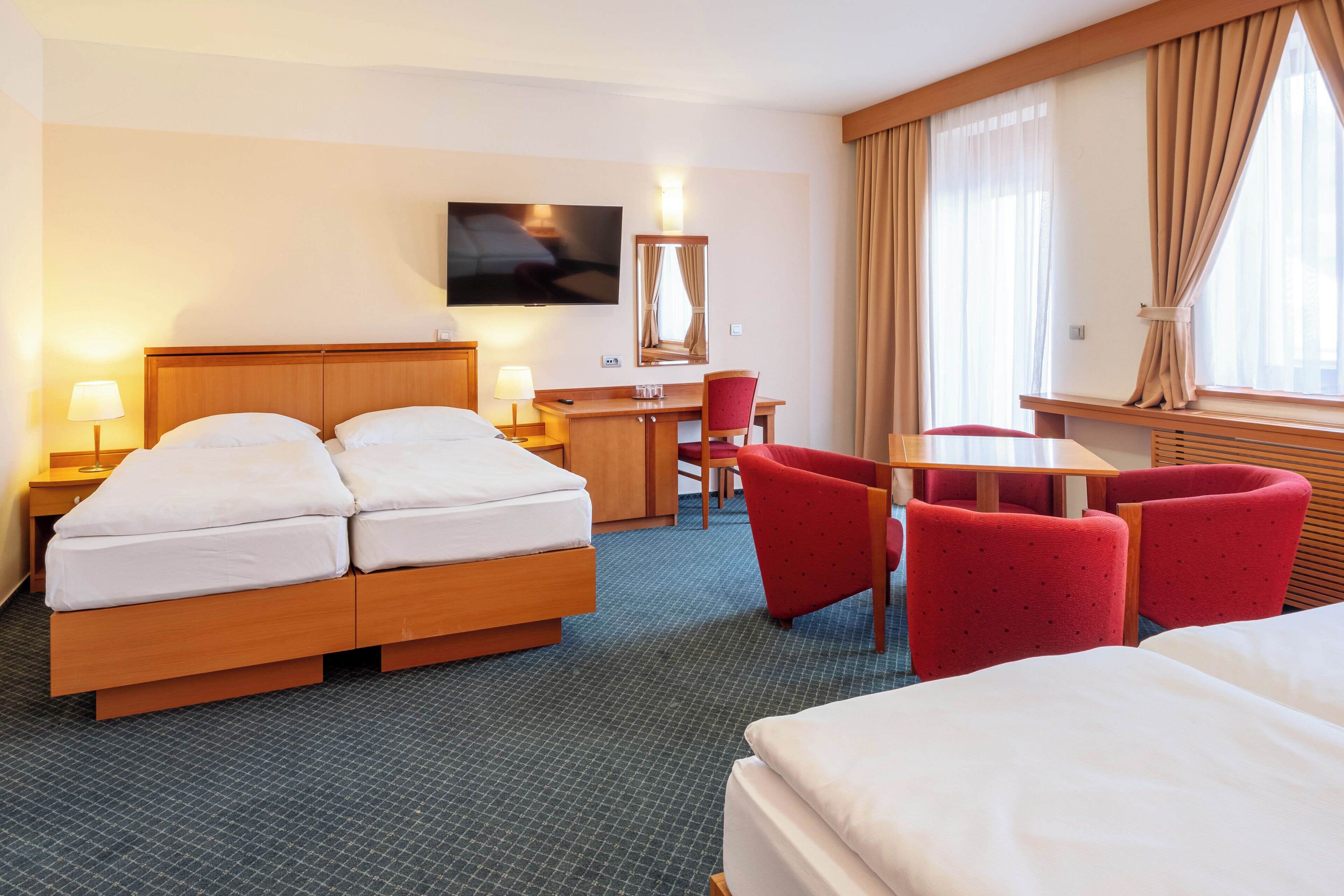 A hotel room with a bed, a desk, a chair, and a TV.
