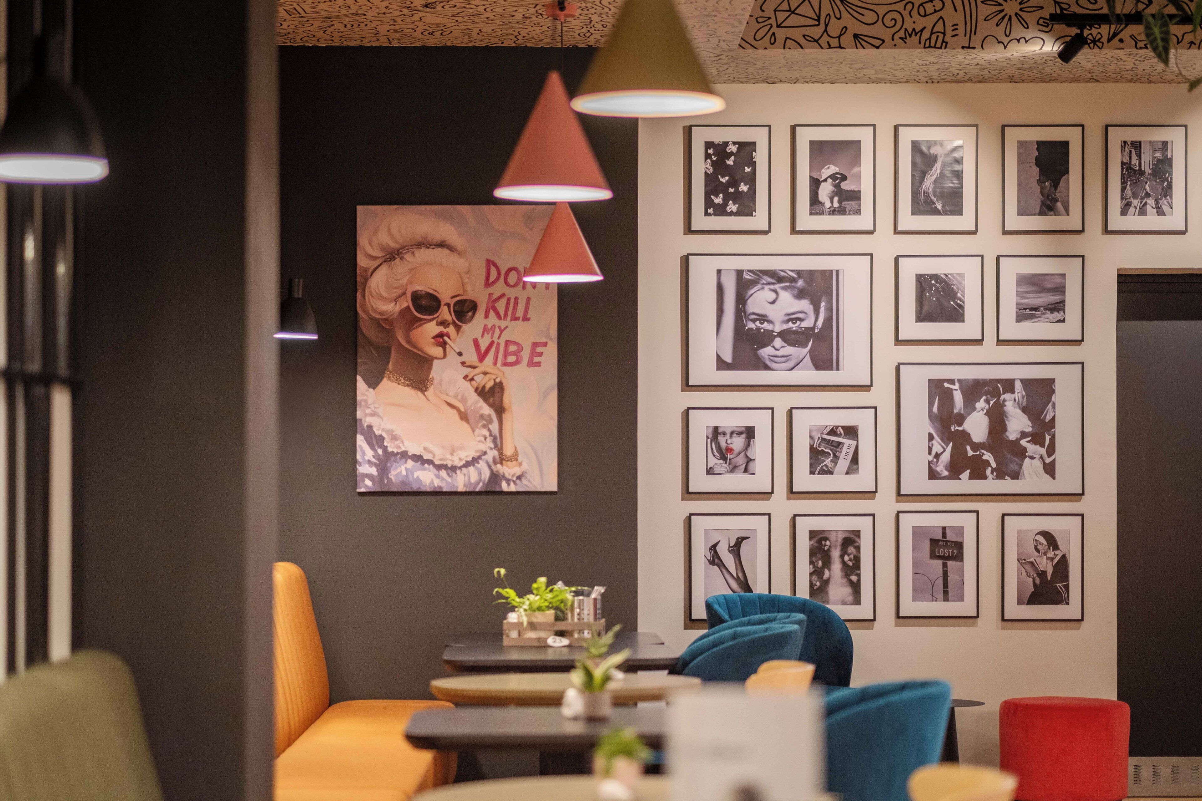 A modern interior with a wall adorned with framed photographs, a prominent poster, and a variety of seating arrangements including a blue chair and a red ottoman.