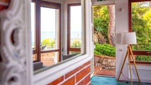 A room with a view of the sea, a balcony with outdoor furniture, and a standing lamp.