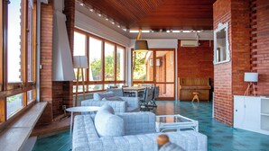 A spacious living area with a large gray sofa, a dining table, and a kitchen area with a brick wall and large windows.