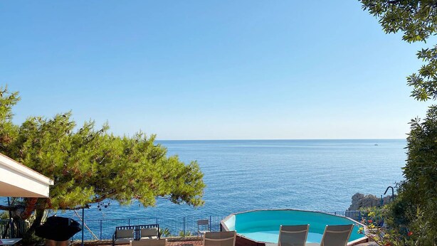 A poolside area with a view of the sea, outdoor seating, and a barbecue grill.