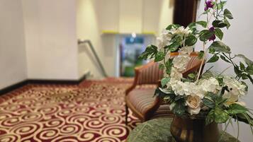 Une pièce avec un tapis à motifs, une chaise en bois et une plante en pot ornée de fleurs blanches.
