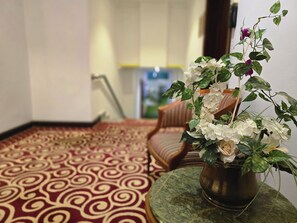 A room with a patterned carpet, a wooden chair, and a potted plant with white flowers. - Taj Celine Hotel (Jeddah)