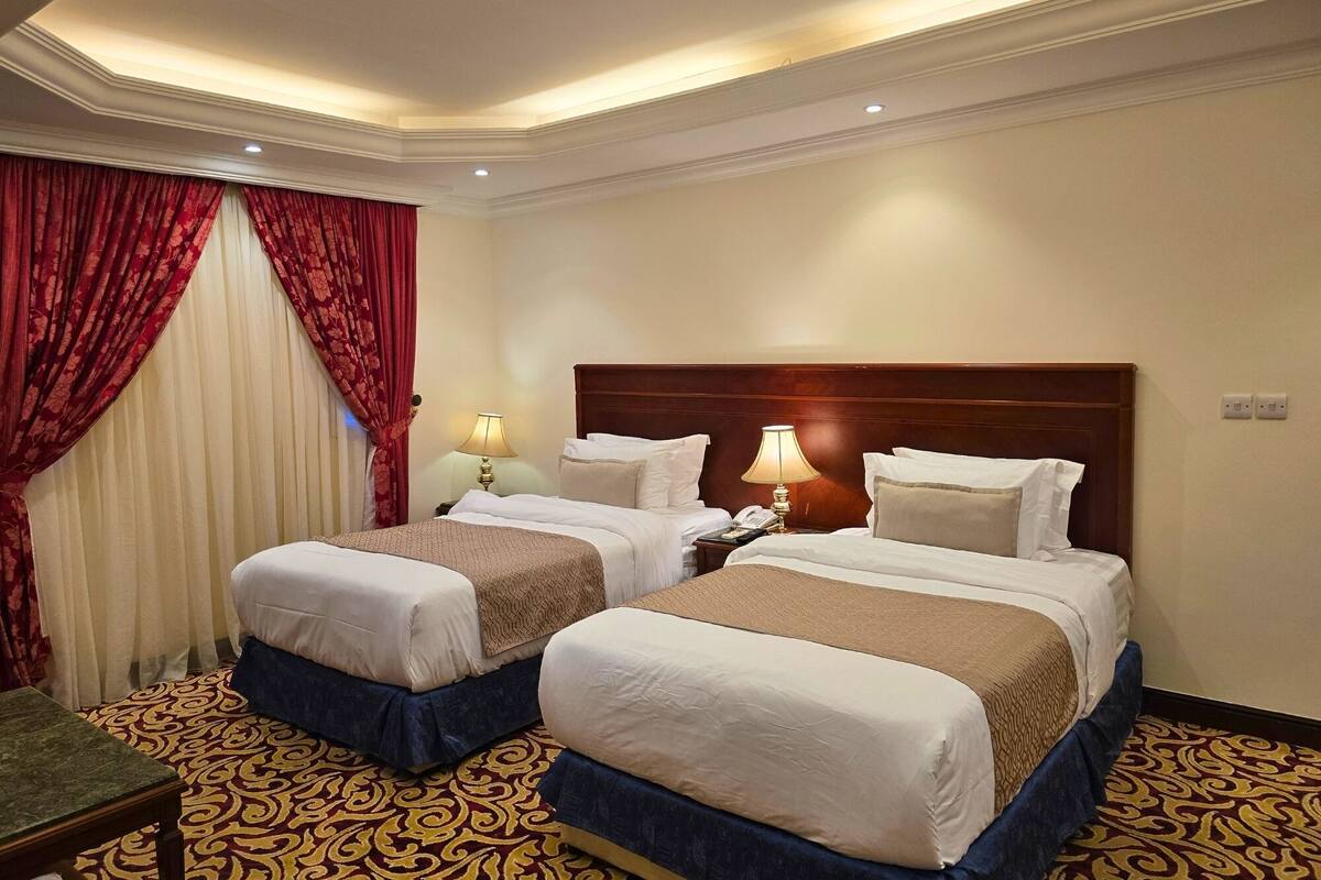 A hotel room with two beds, a patterned carpet, and a red curtain.