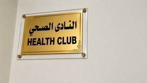 Un letrero con texto en árabe y las palabras en inglés 'HEALTH CLUB' en una pared.