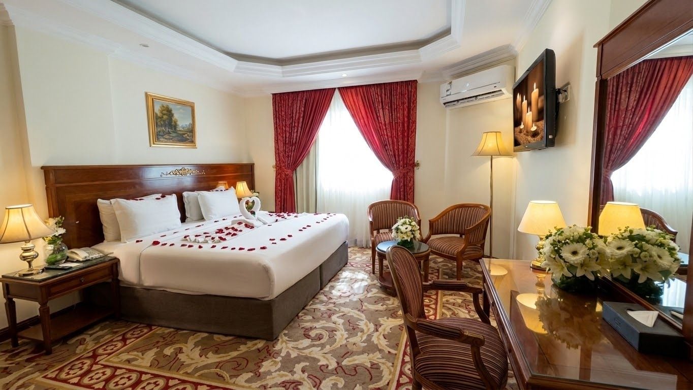 Een hotelkamer met een groot bed, twee nachtkastjes, een zithoek met een stoel en een klein tafeltje, en een grote spiegel.