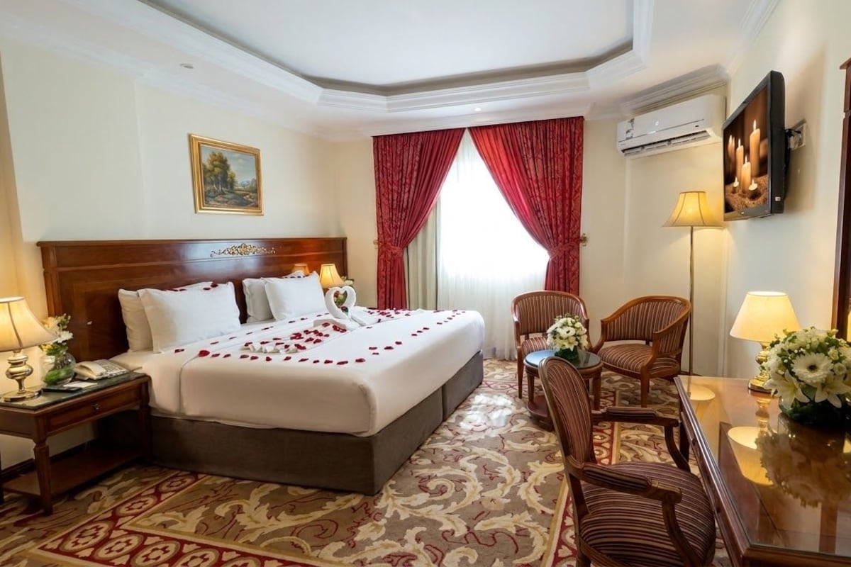 A hotel room with a large bed, two bedside tables, a sitting area with a chair and a small table, and a large mirror.