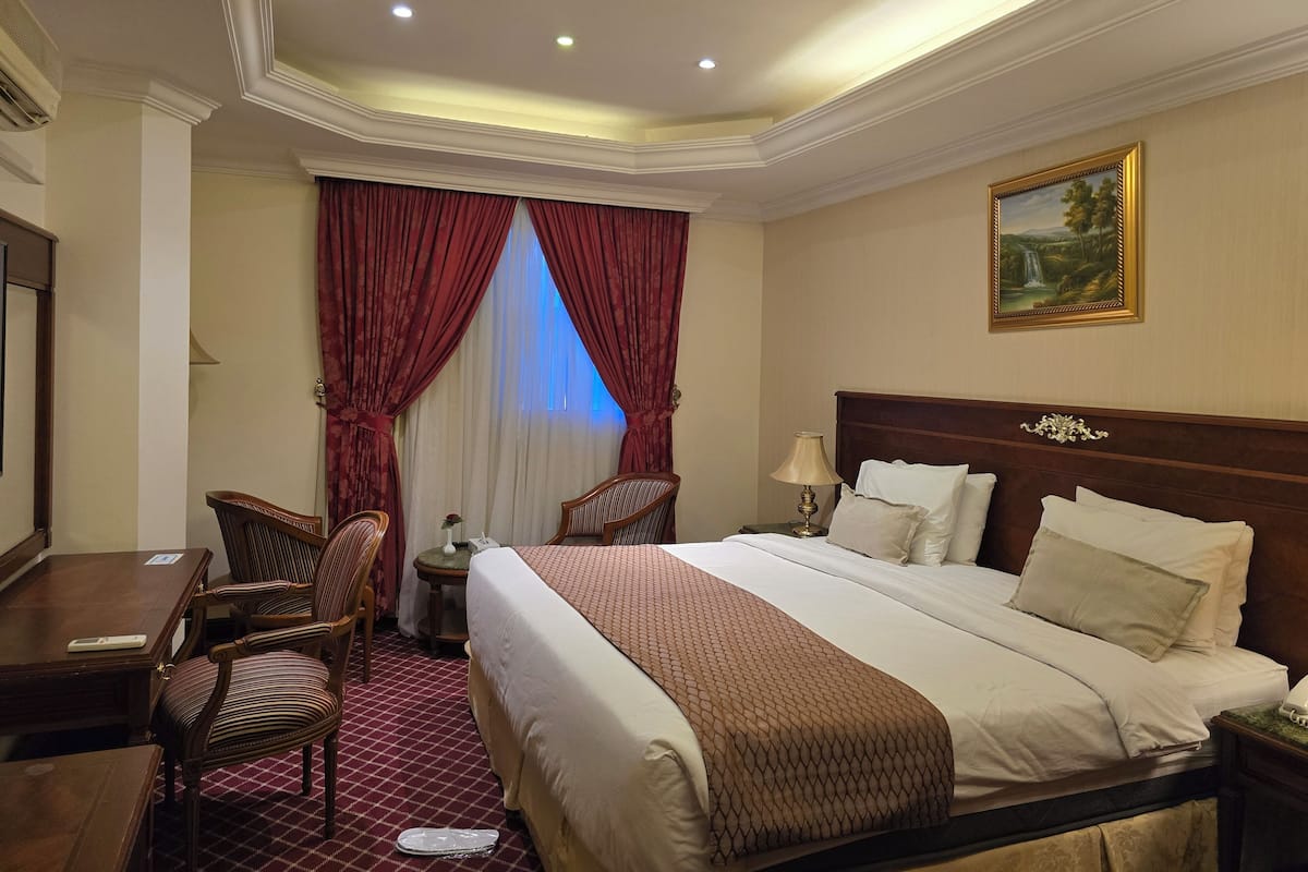 A hotel room with a large bed, two chairs, a desk, and a painting on the wall.