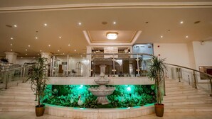 A grand lobby with a central fountain, multiple staircases, and potted plants.