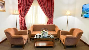 Quarto com sofá, duas poltronas, mesa de centro e televisão na parede.