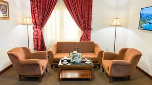 A room with a sofa, two armchairs, a coffee table, and a TV on the wall. - Taj Celine Hotel (Jeddah)