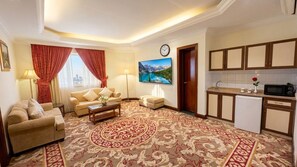 A living room with a sofa, a coffee table, and a television. There is a kitchen area with cabinets and a microwave. - Taj Celine Hotel (Jeddah)