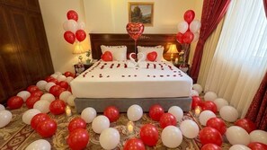 A hotel room with a bed adorned with rose petals, surrounded by red and white balloons, and a heart-shaped balloon with 'Happy Honeymoon' written on it. - Taj Celine Hotel (Jeddah)