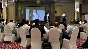 A conference room with attendees seated at round tables, a presentation screen, and a speaker at the front. - Taj Celine Hotel (Jeddah)