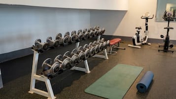 A gym with weightlifting equipment, exercise machines, and a yoga mat.