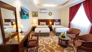 A hotel room with two beds, a sitting area with a table and chairs, a large mirror, and artwork on the walls. - Taj Celine Hotel (Jeddah)
