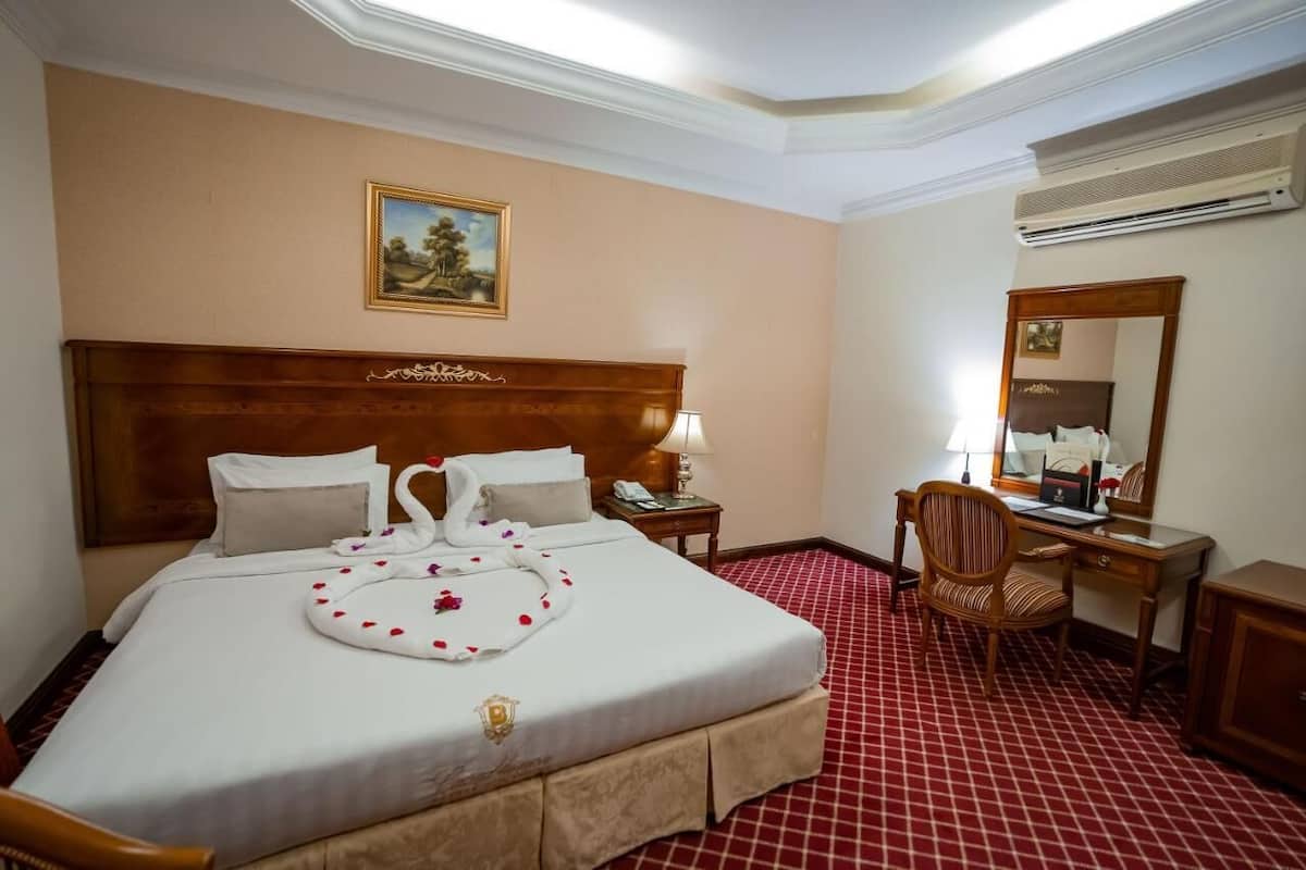 A hotel room with a large bed, a desk, a chair, a mirror, and a painting on the wall.