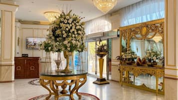 Un hall d’entrée luxueux, agrémenté d’un imposant lustre, d’un grand miroir et d’un arrangement floral disposé sur une table en verre.
