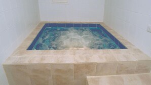 A rectangular hot tub with a blue interior, surrounded by beige tiles.