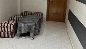 A small room with a tiled floor, a wooden door, and a table with a patterned tablecloth. - Apartment sidi rahhal near beach (Sidi Rahal)
