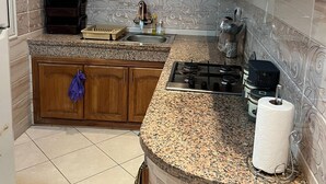 A kitchen with wooden cabinets, granite countertops, a gas stove, and a sink. - Apartment sidi rahhal near beach (Sidi Rahal)