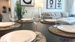 A dining area with a table set for four, including plates, glasses, and cutlery. There are abstract art pieces on the wall and a sofa in the background.