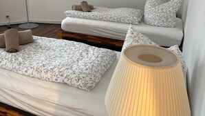 Quarto com duas camas, cada uma com uma colcha florida e almofadas combinando. Há um abajur com cúpula bege ao lado direito da cama.