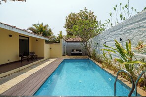 A rectangular swimming pool with a wooden deck, a bench, and a small table.