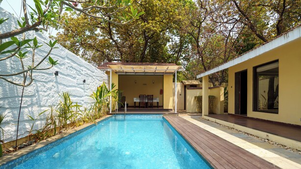 Une piscine rectangulaire dotée d’une terrasse en bois, entourée d’un mur blanc et d’arbres.