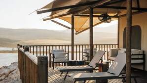 Une terrasse en bois, dotée de chaises longues et d’un auvent, qui offre une vue sur une étendue d’eau et sur des collines lointaines.