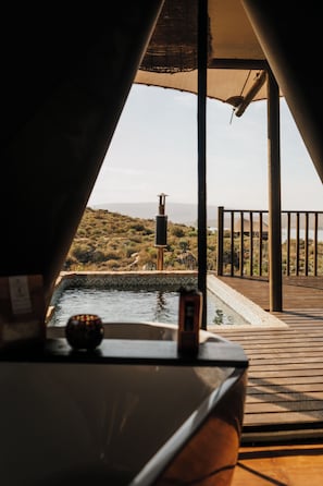 A pool area with a view of a hilly landscape, a wooden deck, and a metal railing.