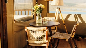 Een tentkamer met een ronde tafel, rieten stoelen, een lamp en een vaas met bloemen.